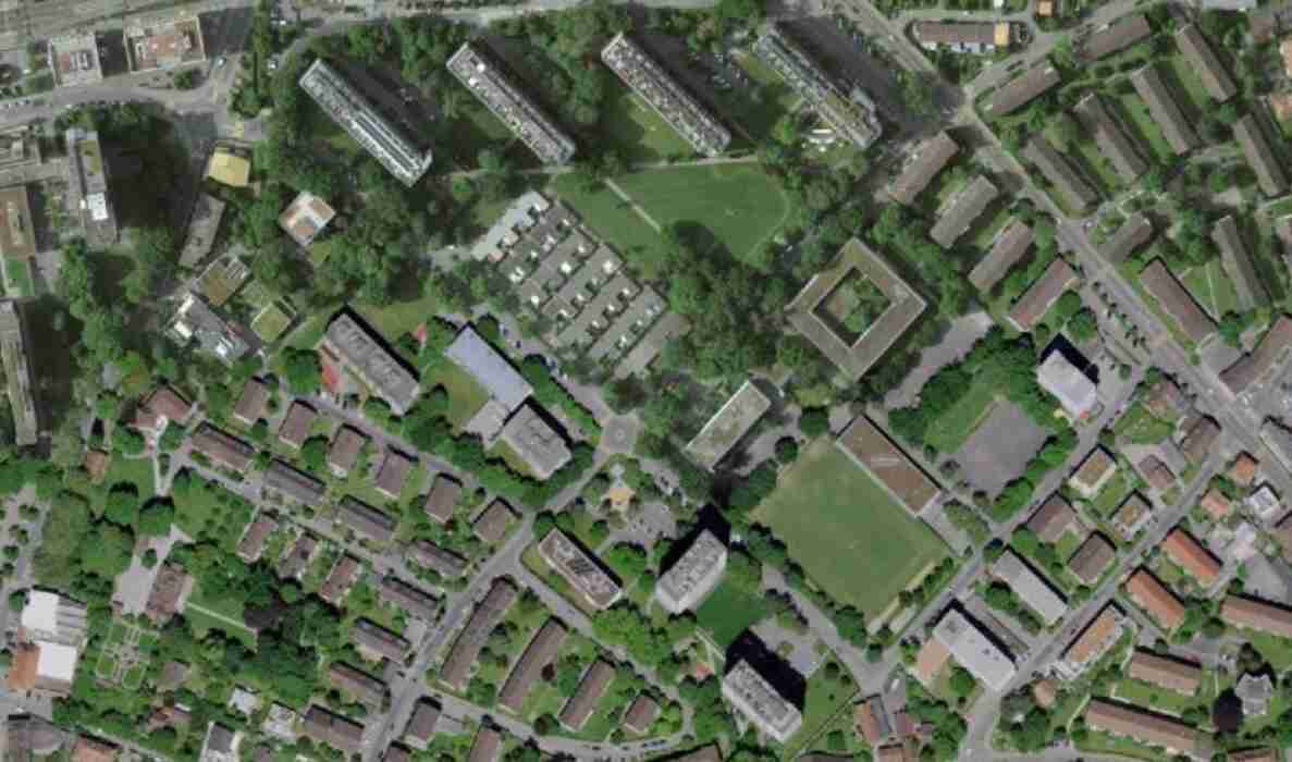 Luftbild des Quartiers Schwabgut in Bern mit Wohnzeilen, Punktbauten und einem markanten ringförmigen Gebäude im Zentrum. Erschlossen durch mehrere Quartierstrassen mit Erschliessungsfunktion für Fussgänger und Fahrzeuge. Grosszügige Grünflächen, Sportplatz sowie Baumreihen entlang der Wege prägen die Umgebung. Keine Verkehrsteilnehmenden oder Verkehrssignale erkennbar (Quelle: @swisstopo 2024).