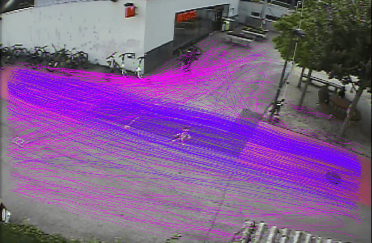 Übersichtsaufnahme eines Vorplatzes mit Velostation, überlagert mit violetten und pinken Linien, welche die Bewegungswege des Fuss- und Veloverkehrs quer über den Platz visualisieren. Eine gehende Person ist inmitten des dichten Linienbündels erkennbar, im Hintergrund stehen Velos an Ständern sowie eine Sitzbank unter Bäumen.
