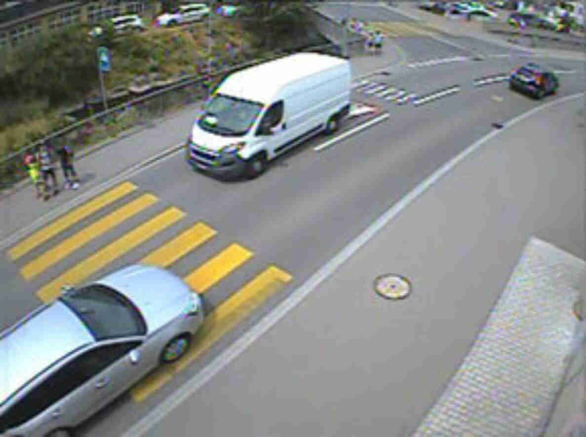 Kreuzungsbereich an der Hauptstrasse K248 in Niederlenz mit weissem Lieferwagen und silbernem Personenwagen im Verkehr. Fussgängerstreifen führt über die Fahrbahn, mehrere Personen befinden sich am Strassenrand nahe des Zebrastreifens. Fahrbahnmarkierungen und Randlinien sind gut sichtbar, die Strasse ist mehrspurig mit ausreichend Platz für Fahrzeuge und Fussverkehr.