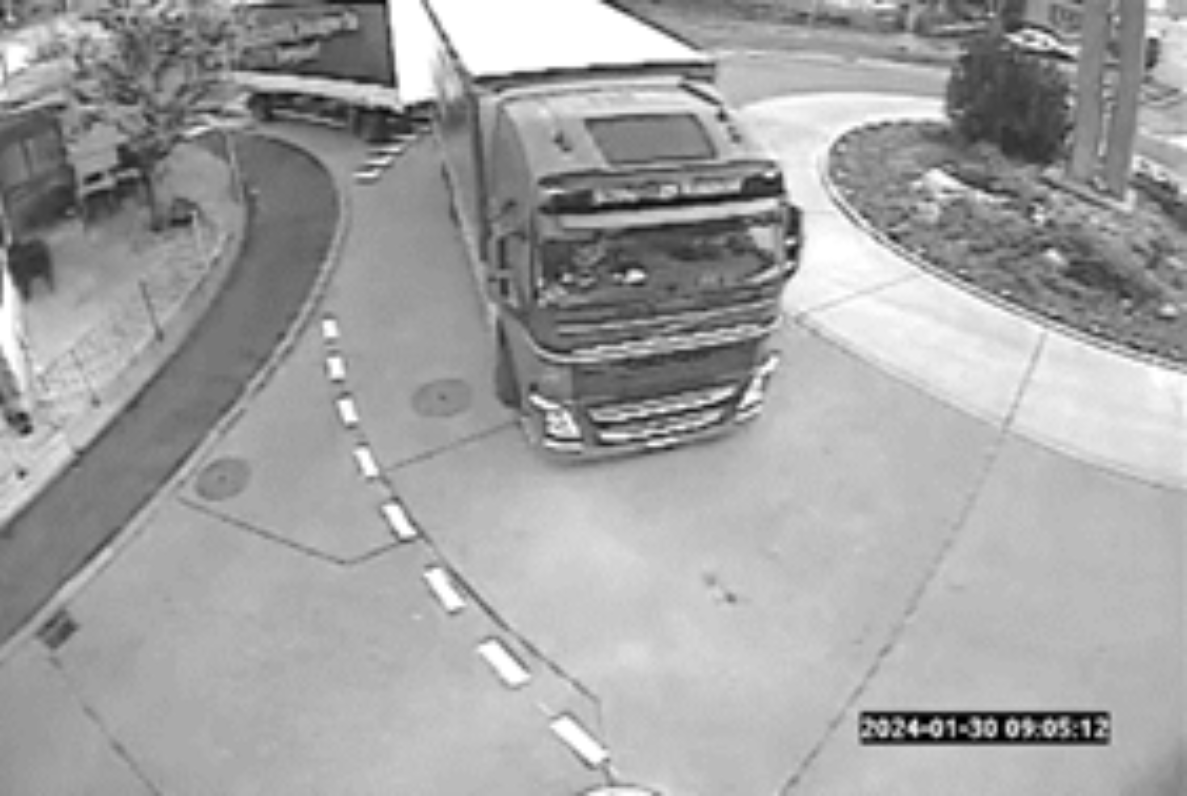 Überwachungskamera-Ansicht (Schwarz-Weiss) auf Kreisverkehr beim Bahnhof Ramsei: Lastwagen mit Anhänger durchfährt die Kreisverkehrsfahrbahn, gekennzeichnet mit weisser Leitlinie. Gepflasterter Mittelbereich mit Bepflanzung. Zeitstempel unten rechts zeigt Datum und Uhrzeit der Aufnahme. Keine weiteren Verkehrsteilnehmenden sichtbar.