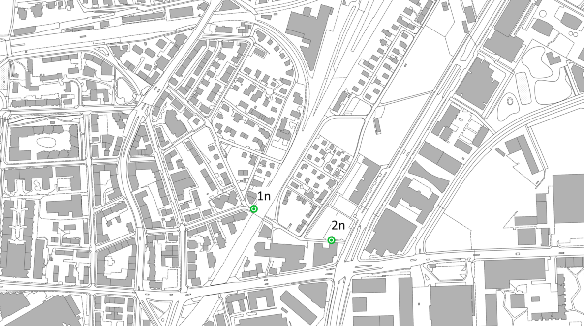 Stadtplan-Ausschnitt von Zuerich-Seebach mit Quartierstrassen und Gebaeudegrundrissen in Grau. Zwei gruen markierte Standorte 1n und 2n kennzeichnen Punkte der Ergaenzungserhebung entlang einer Hauptstrasse, die zu einer grossen Kreuzung im unteren Bildbereich fuehrt. Keine Fahrzeuge oder Personen sichtbar, reine schematische Kartendarstellung zur Standortbestimmung von Verkehrsmessungen.